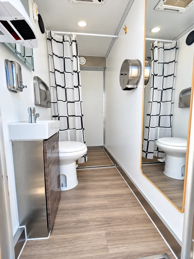 Shower and restroom trailer interior with a sink, toilet and curtained shower